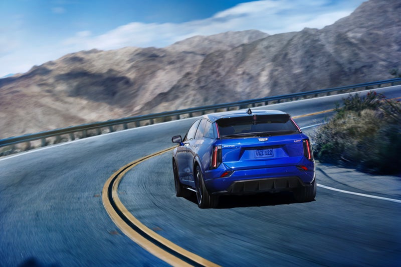 Rear View of a Blue 2026 OPTIQ-V Driving on a Curve of a Mountain Row | Courtesy Cadillac Broussard in Broussard LA