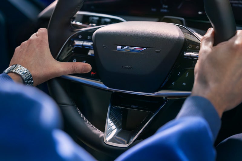 Close-up of a Man About to Press the V-Button on the 2026 OPTIQ-V Steering Wheel | Courtesy Cadillac Broussard in Broussard LA